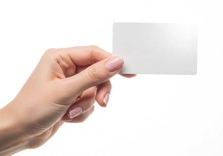 A close-up view shows a woman's hand, featuring neatly manicured nails, delicately holding a small, blank white rectangular card against a pure white backdrop.の素材
