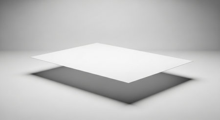 A single, clean, white sheet of paper suspended in the air, creating a distinct shadow on the surface below, suggesting lightness and space.の素材