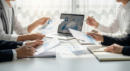 A group of professionals collaborates, reviewing financial reports and charts on a laptop, strategizing for company growth, and discussing data-driven insights in a meeting.の素材