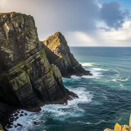 A stunning panoramic view of rugged sea cliffs dramatically plunging into the deep blue ocean. White foamy waves crash against the rocky shoreline under a dynamic, cloudy sky.の素材