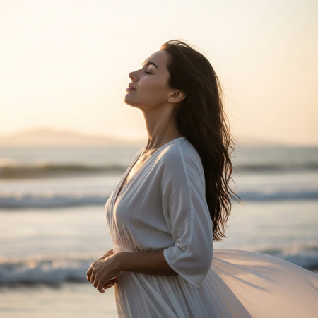 A woman with eyes closed breathes deeply, bathed in the warm glow of a sunset on a tranquil beach.の素材