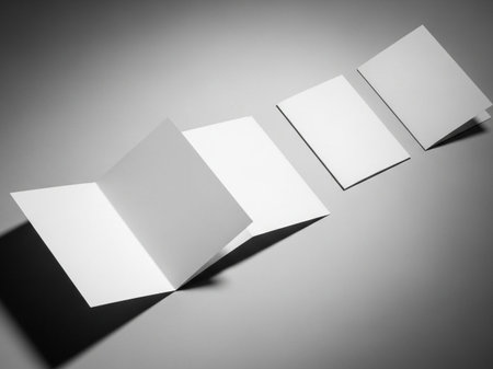 A black and white photo of three white business cards on a gray surface with shadows cast to the left, creating depth and dimensionの素材