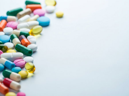 Assorted multicolored pills and capsules on a light blue background, representing health and medicine with a variety of colors and shapesの素材
