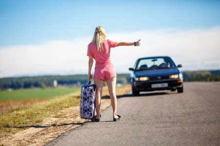 young woman hitch-hiking on a road at the fieldsの写真素材
