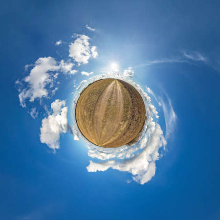 green tiny planet in blue sky with sun and beautiful clouds. Transformation of spherical panorama...