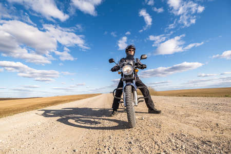 man in a black uniform on bike against the backdrop of panorama of field and blue sky. motorcycle travel conceptの写真素材