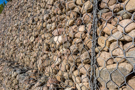 engineering structure made of stones behind metal wire netting to strengthen the river bank near the road bridgeの写真素材