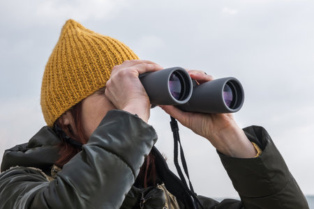 female ornithologist birdman watches birds with binoculars on dirt gravel road against a background of a stormy skyの写真素材