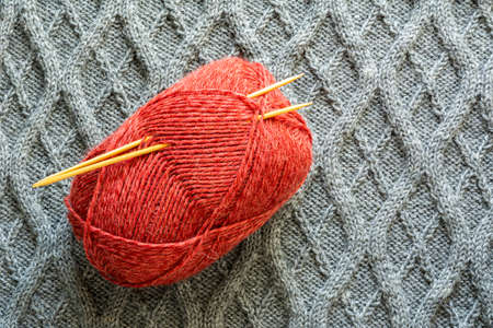 The ball of yarn with knitting needles on the knitted day blanket