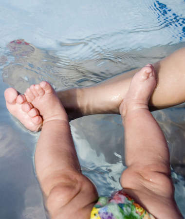 Young child's foot with two baby feet in pool waterの写真素材