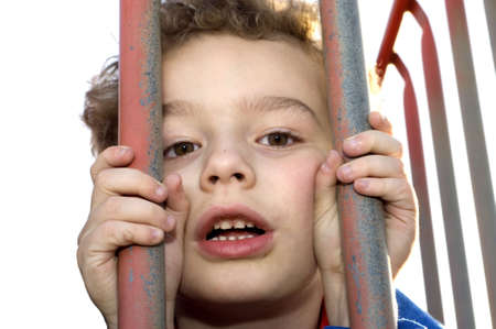 Young boy playing prisoner behind bars at playgroundの写真素材