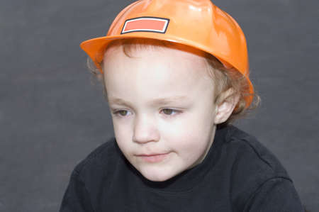 Young boy wearing orange construction hat against black backgroundの写真素材