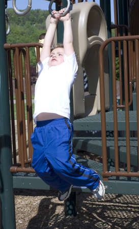 Young boy hanging from playground rings with fear in eyes