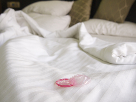 Messy bed in a hotel with a pink condomの写真素材