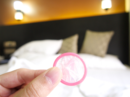 Holding a condom in a hotel with a messy bedの写真素材