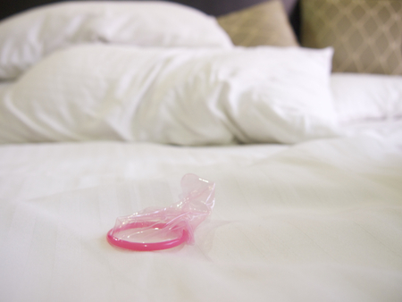 Messy bed in a hotel with a pink condomの写真素材