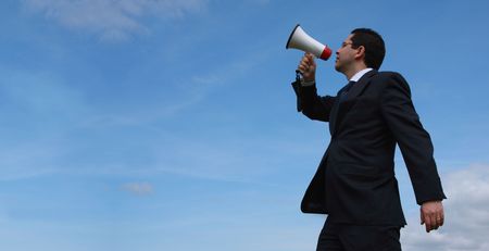 Businessman speaking with a megaphone with the blue sky as background (wide format photo)の写真素材