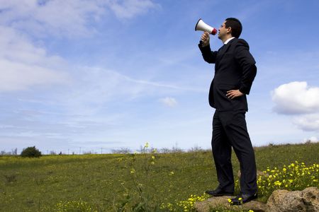 Businessman speaking with a megaphone in a fieldの写真素材
