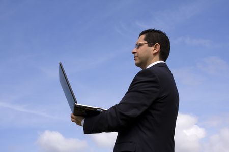 Businessman with a laptop and blue sky as backgroundの写真素材