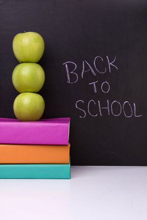 apple over a stack of books next to a chalkboardの写真素材