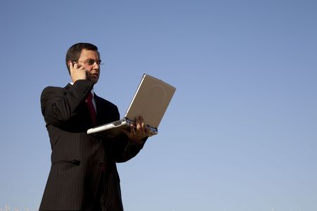 businessman talking on the cellphone and holding a laptop on outdoorの写真素材
