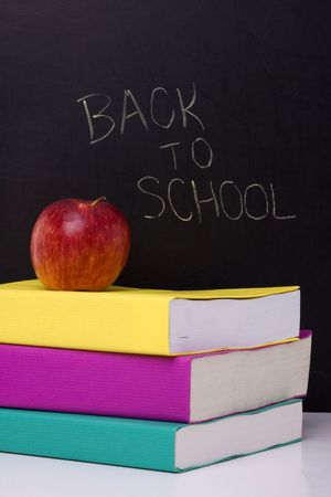 apple over a stack of books next to a chalkboardの写真素材