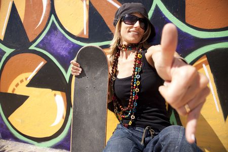 cool skateboard woman next to a graffiti wall. The Graffiti is illegal art in a public park.の写真素材