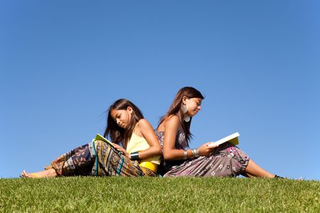 two young sisters reading books at the parkの写真素材