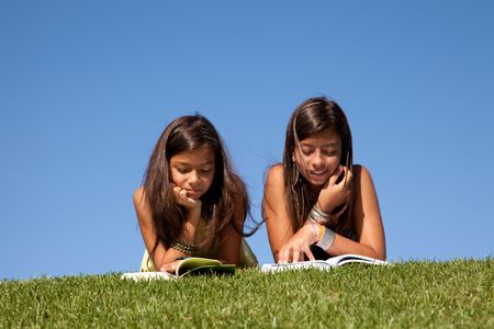 two young sisters reading books at the parkの写真素材