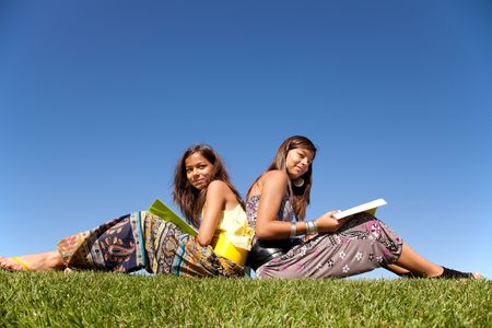 two young sisters at the park reading a bookの写真素材
