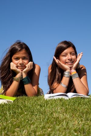 two young sisters at the park reading a bookの写真素材