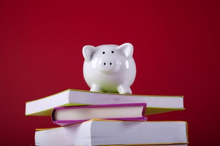 piggy bank over a stack of colorful books with a red backgroundの写真素材