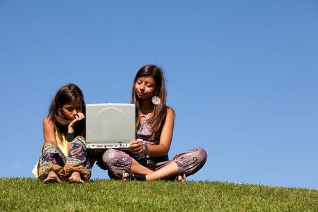 two young sisters using the internet at the park on her laptopの写真素材