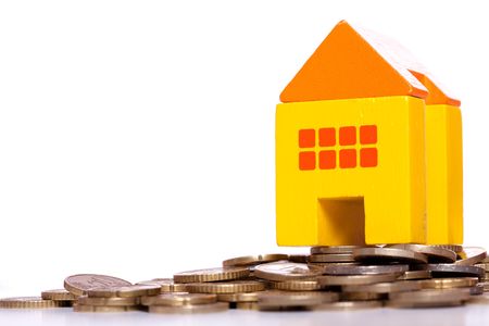 yellow toy house over a lot of golden coins (isolated on white)の写真素材
