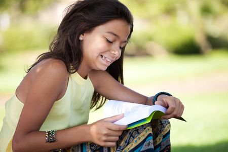little girl relaxing next to a tree reading a bookの写真素材