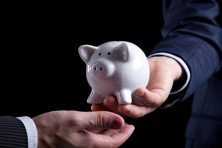 Businessman giving a piggy bank to you (isolated on black)の写真素材
