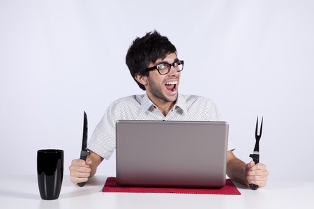 Young men at dinner table eating technology with a funny face expressionの写真素材