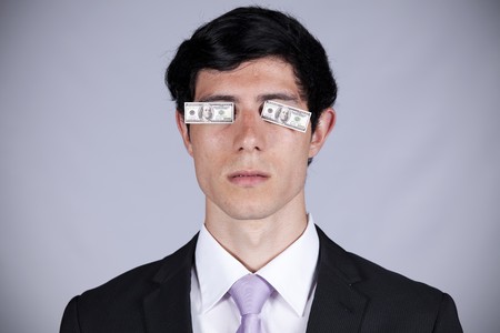 Young businessman with little dollar bills covering his eyesの写真素材