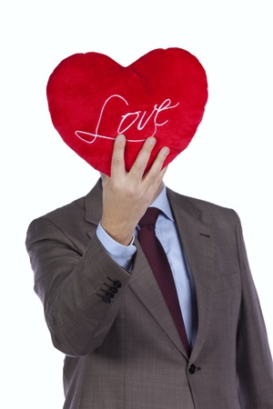 Businessman holding a red pillow with a heart shape in front of his head (isolated on white)の写真素材