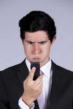 Businessman with a angry face expression looking to his mobile phone (isolated on gray)の写真素材