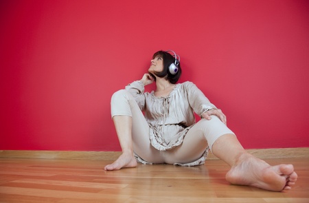 Woman listening to music with headphones sited on the floor at homeの写真素材