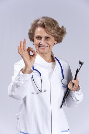 Happy senior doctor gesturing ok to you (isolated on gray)の写真素材