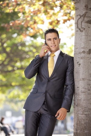 Successful and handsome businessman talking at his cellphone next to a treeの写真素材