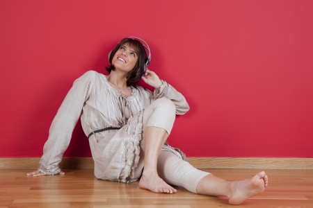 Woman listening to music with headphones sited on the floor at homeの写真素材
