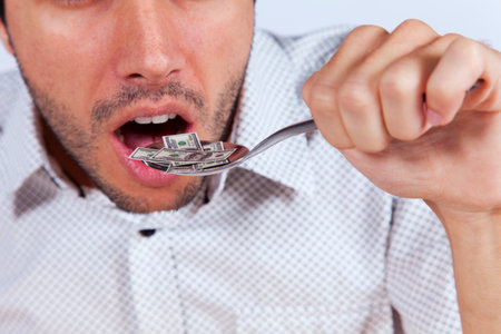 Man eating money at a plate with a fork and a knife