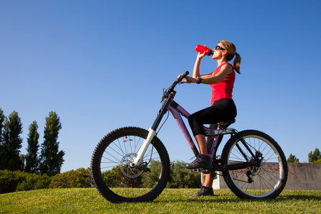 young woman on a bicycle drinking water at the parkの写真素材