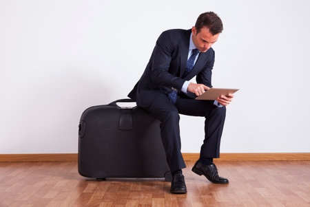 Businessman sitting on a travel luggage using a digital tabletの写真素材