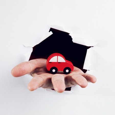 hand holding a red car through a hole in a white paper backgroundの写真素材