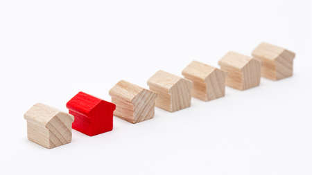 Tiny wooden toy houses in a row, one of them painted red, white backgroundの写真素材