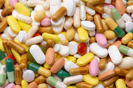 Medicines (tablets, capsules, pills) of different kinds, sizes and colors, piled up in bulk....